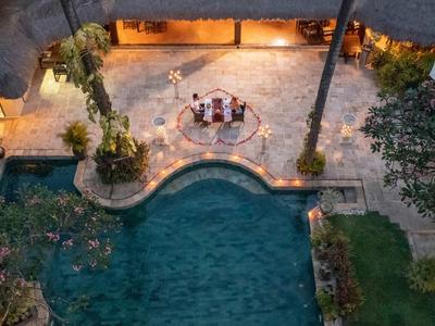 Ein beleuchteter Pool mit geschwungener Form, umgeben von Pflanzen und Terrassenbereich bei Abendlicht.