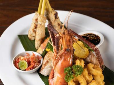 Ein Teller mit Garnelen, Calamari, Gemüse und kleinen Schalen mit Dips, dekorativ angerichtet.