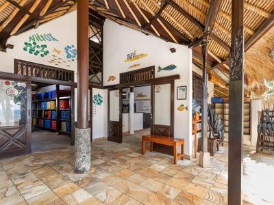 Rezeption und Bibliothek mit steinernen Böden und Holzstühlen in einer offenen Lodge mit hohen Dächern.