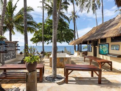 Offener Loungebereich mit Holzmöbeln und Blick auf Palmen und das Meer bei klarem Himmel.