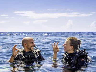 Zwei Taucher zeigen ein OK-Zeichen im Meer während eines Tauchgangs bei klarem Himmel.