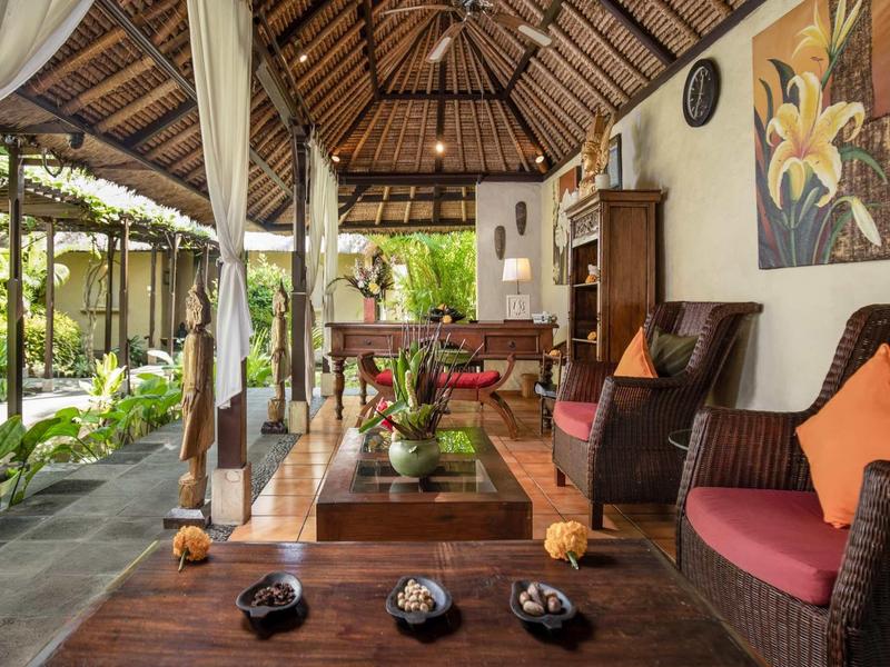 Gemütliche Terrasse mit Holzmöbeln, rotem Sofa, Pflanzen und offenem Dach aus Holz und Stroh.