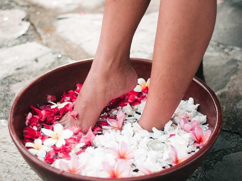 Beine in Schüssel mit Wasser, weißen und roten Blüten auf Steinboden.