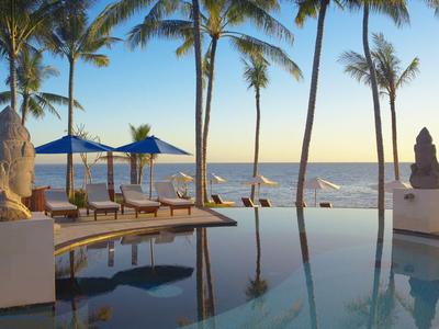 Basen infinity z leżakami, parasolami i palmami na plaży o zachodzie słońca.