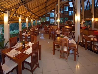 Otwarta restauracja z drewnianymi meblami i strzechą w tropikalnym otoczeniu.