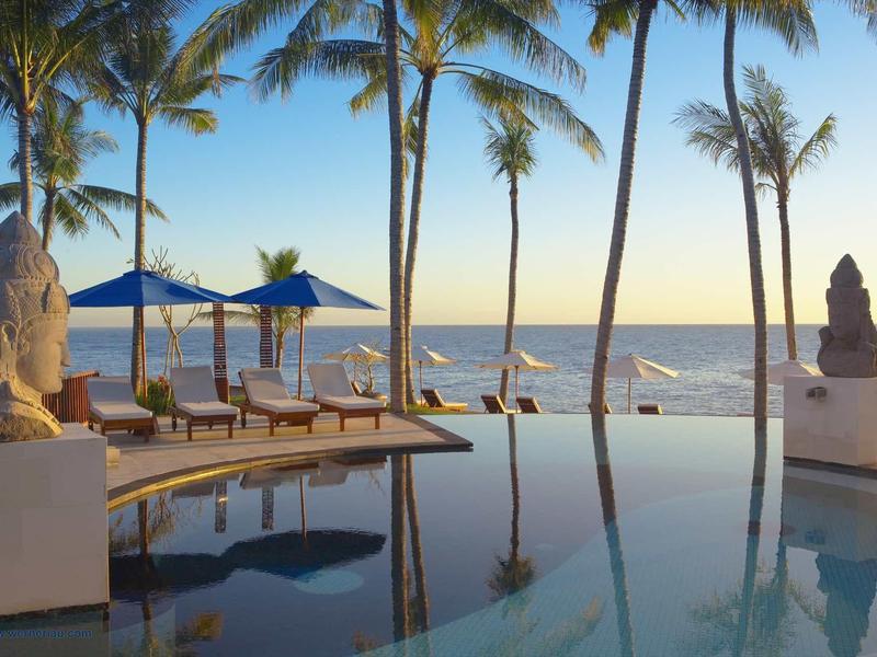 Basen infinity z leżakami i palmami nad morzem o zachodzie słońca.