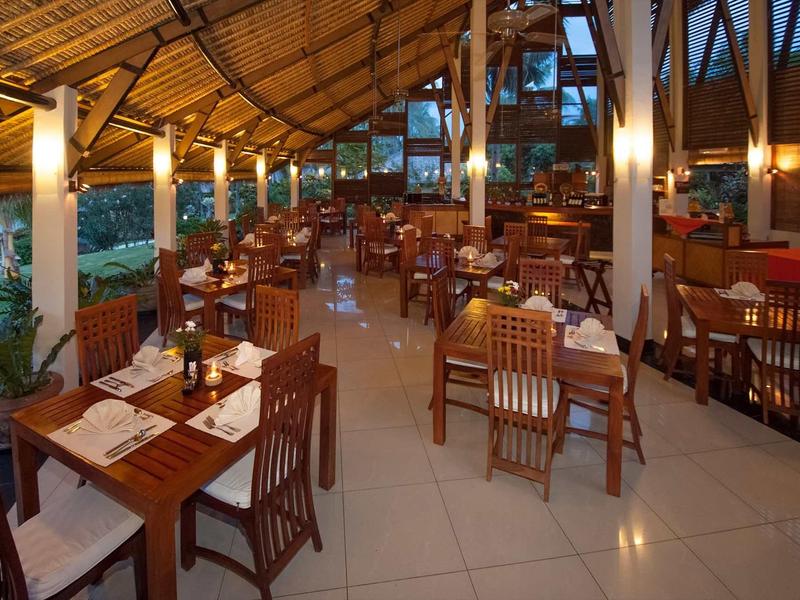 Otwarta restauracja z drewnianymi meblami i strzechą w tropikalnym otoczeniu.