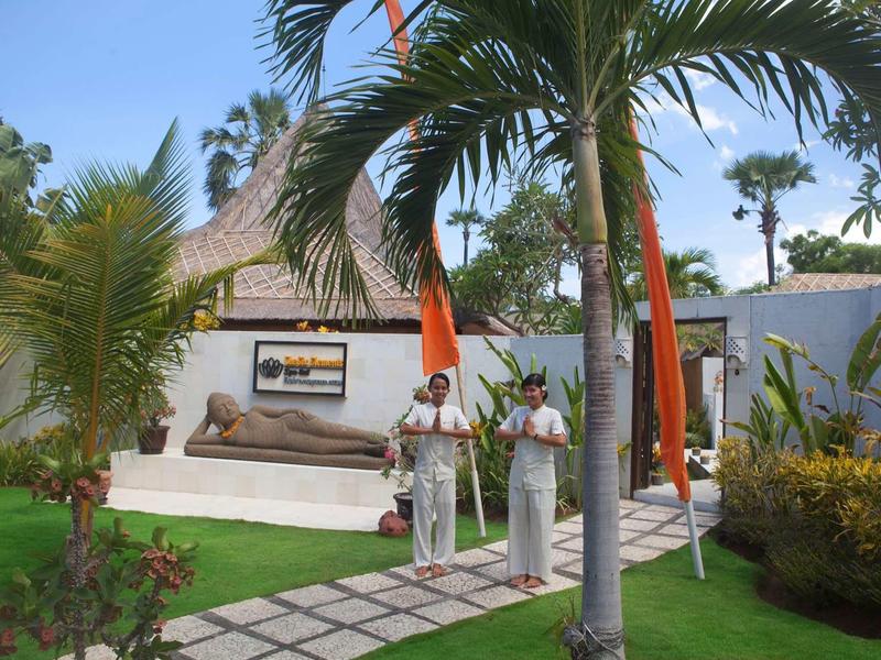 Dwie kobiety w białych strojach stoją w ogrodzie ośrodka z palmami i tropikalną dekoracją.