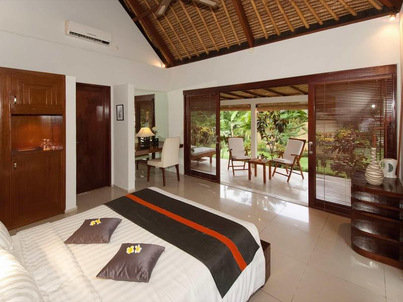 Jasna sypialnia z drewnianym sufitem, łóżkiem i otwartym dostępem do tarasu z widokiem na ogród.