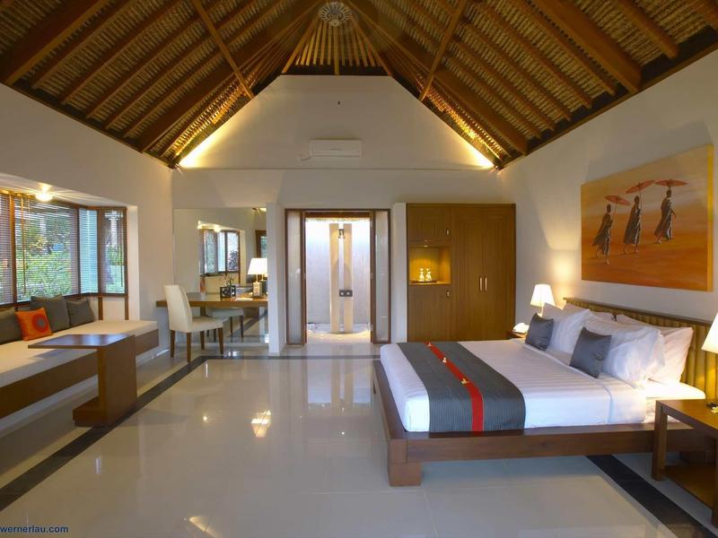 Nowoczesny pokój hotelowy z otwartym sufitem, łóżkiem podwójnym i miejscem do siedzenia z widokiem na zieleń.