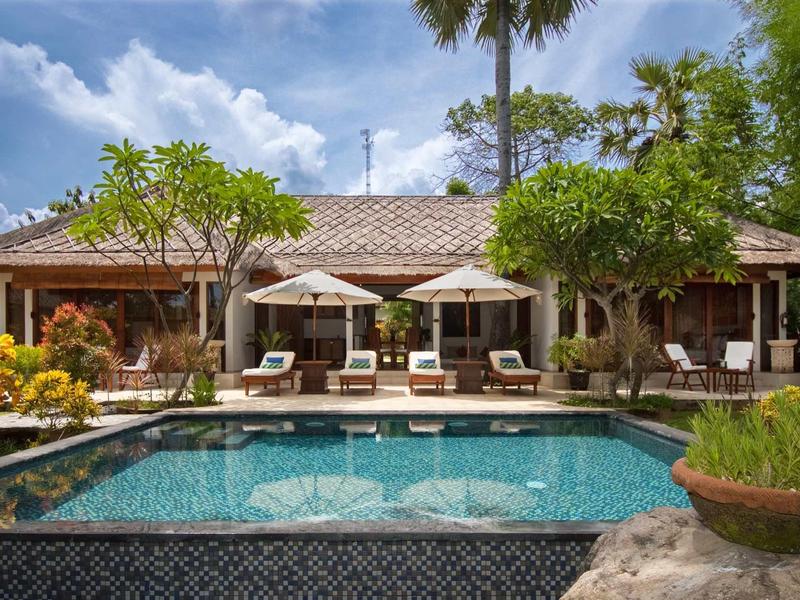 Przytulny dom wakacyjny z basenem, leżakami i parasolami w otoczeniu tropikalnym.