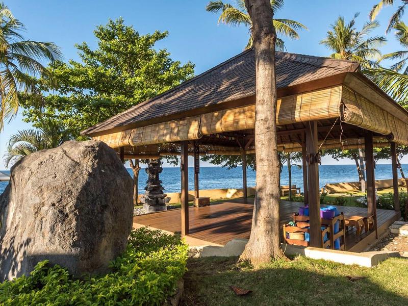 Otwarta altana na plaży z widokiem na morze, otoczona palmami i bujną zielenią.