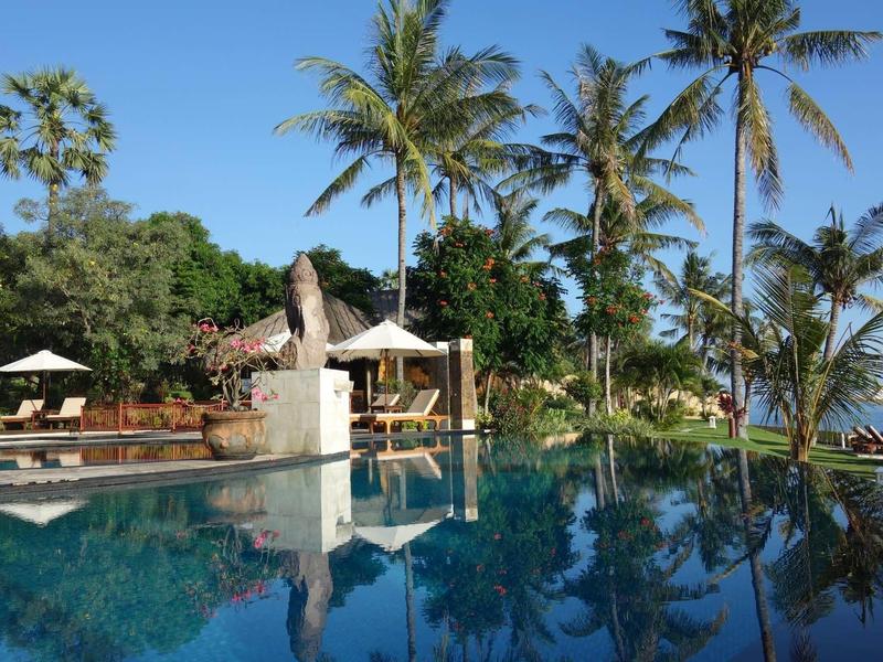 Tropikalny basen hotelowy z palmami i parasolami pod czystym niebieskim niebem.