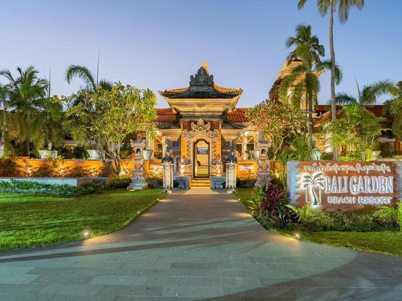 Eingang eines tropischen Resorts mit Palmen, beleuchteten Wegen und dekorativem Tor.