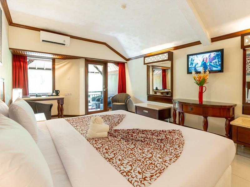 Helles Hotelzimmer mit großem Bett, TV, Schreibtisch und roten Vorhängen, helle Wände und Decke.