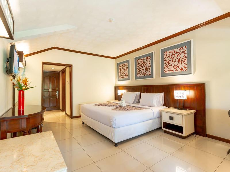 Helles Hotelzimmer mit Doppelbett, Nachttisch, Wanddekoration und Fliesenboden.