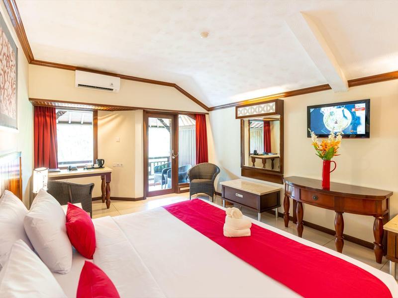 Helles Hotelzimmer mit großem Bett, roten Akzenten, Schreibtisch, TV und Balkon mit Aussicht.