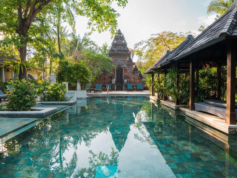 Großer Pool mit klarem Wasser, umgeben von Pavillons und Bäumen, mit Tempel im Hintergrund.