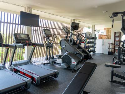 Fitnessraum mit Laufbändern, Ellipsentrainern und Kraftgeräten vor großen Fenstern.