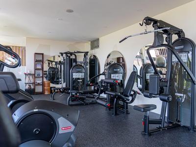 Innenansicht eines Hotel-Fitnessraums mit verschiedenen Trainingsgeräten und natürlichem Licht.