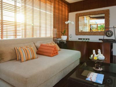 Gezellige woonkamer met beige bank, kussens, glazen tafel en decoratieve spiegel in hotelkamer.