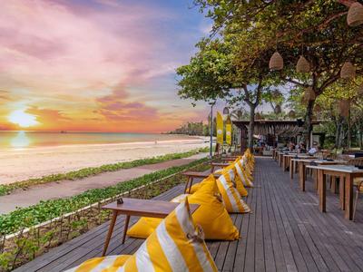 Zonterras met kussens en zeezicht bij zonsondergang op een hotelstrand.