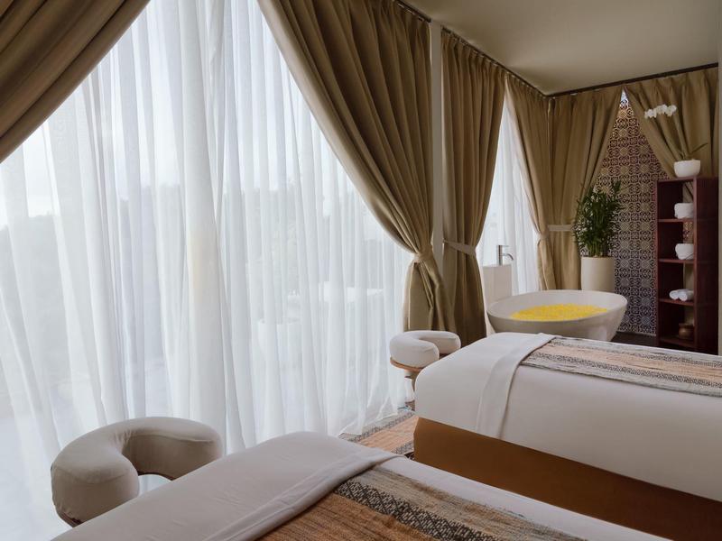 Lichte spa-kamer met massagetafels, gordijnen en grote spiegel.