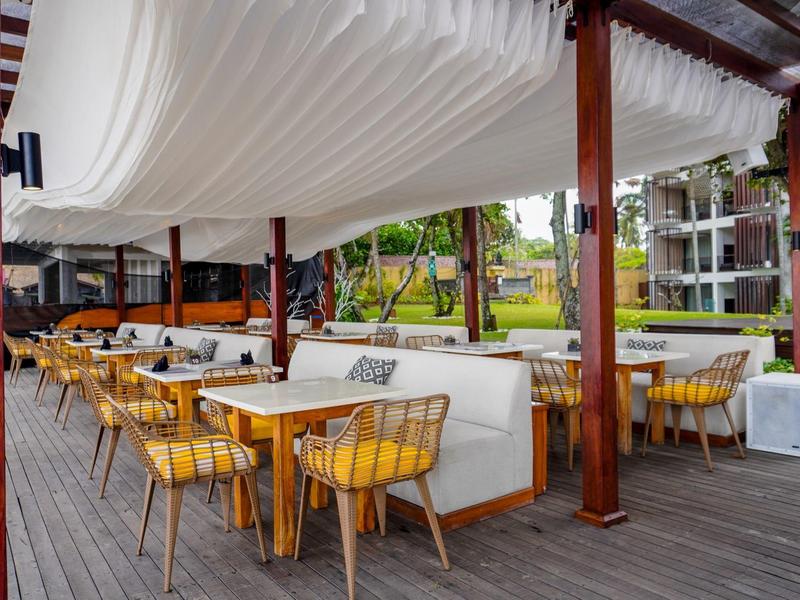 Buitengebied van een modern hotel met gele stoelen en witte luifels op een houten terras.