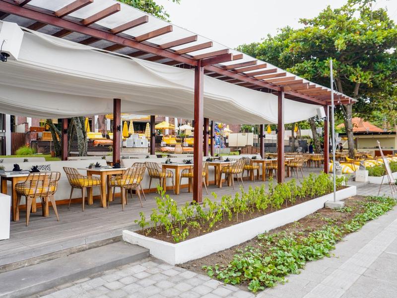 Open buitengedeelte van restaurant met gedekte tafels en houten dak in hotelomgeving.