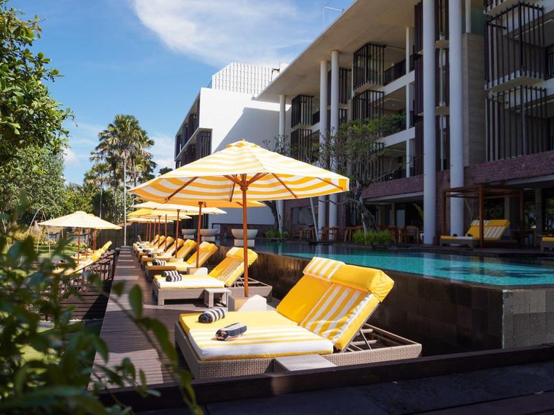 Moderne hotelterras met zwembad, ligstoelen en gele parasols op een zonnige dag.