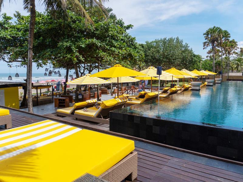 Luxe zwembad met gele ligbedden en parasols aan zee.