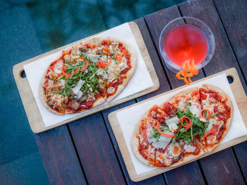Twee pizza's op houten planken met een rood drankje op een donkere tafel.