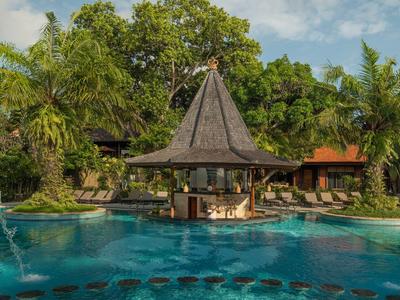 Una piscina exótica con un bar cubierto y vegetación exuberante al fondo.