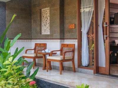 Patio d'hôtel confortable avec deux chaises en bois, petite table et plantes vertes luxuriantes.