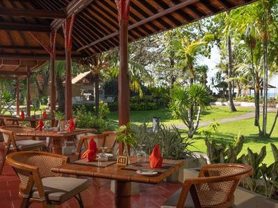 Espace repas extérieur avec tables et chaises en bois donnant sur un jardin luxuriant et des palmiers.