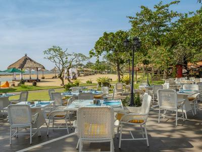 Espace extérieur avec tables et chaises entouré de verdure sous un ciel dégagé.