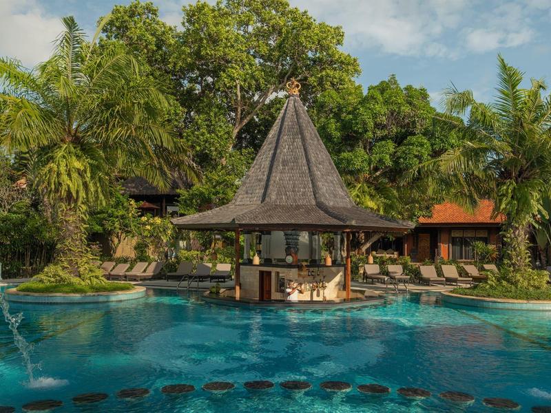 Bar au bord de la piscine avec toit de chaume entouré d'une végétation tropicale luxuriante.