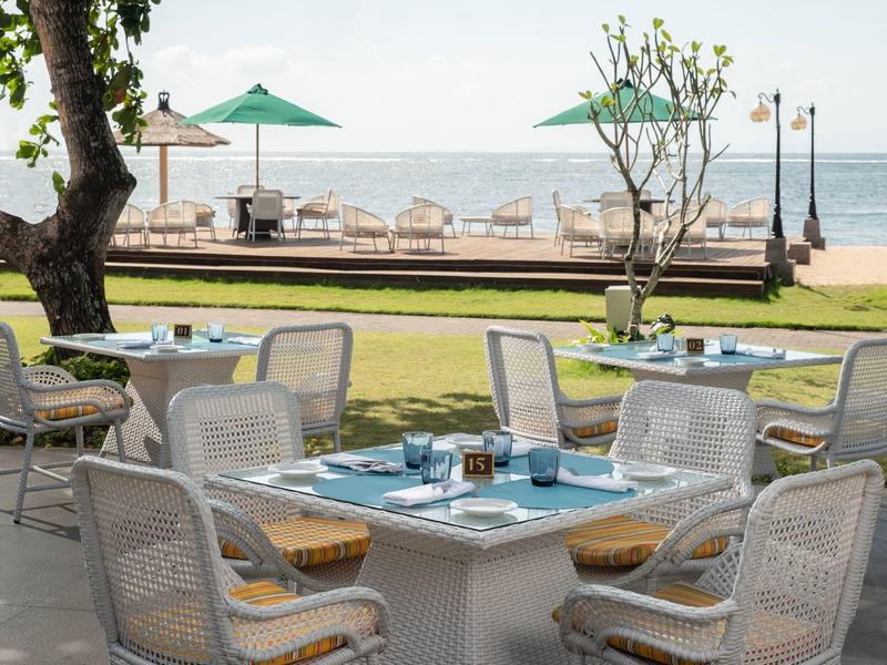 Espace repas en plein air avec tables, chaises et parasols près de la plage et de l'océan.