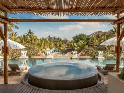 Okrągły jacuzzi na zadaszonym tarasie z widokiem na basen i tropikalne rośliny.