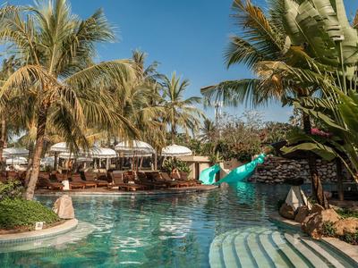 Strefa basenowa z zjeżdżalnią wodną i palmami w tropikalnym hotelu w słoneczny dzień.