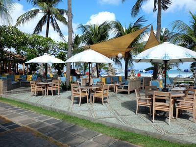 Restauracja na świeżym powietrzu z drewnianymi stolikami, parasolami i palmami przy plaży.