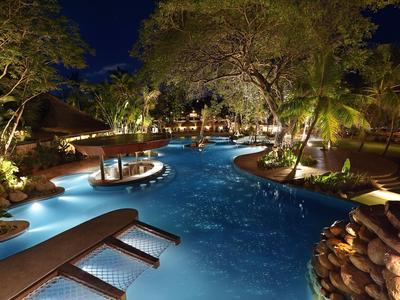 Área de piscina iluminada con tumbonas y árboles en un ambiente nocturno de resort