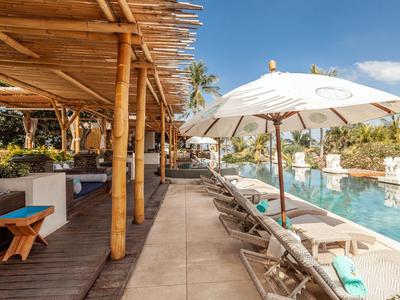 Área de piscina acogedora con tumbonas, sombrillas y techo de bambú bajo un cielo soleado.