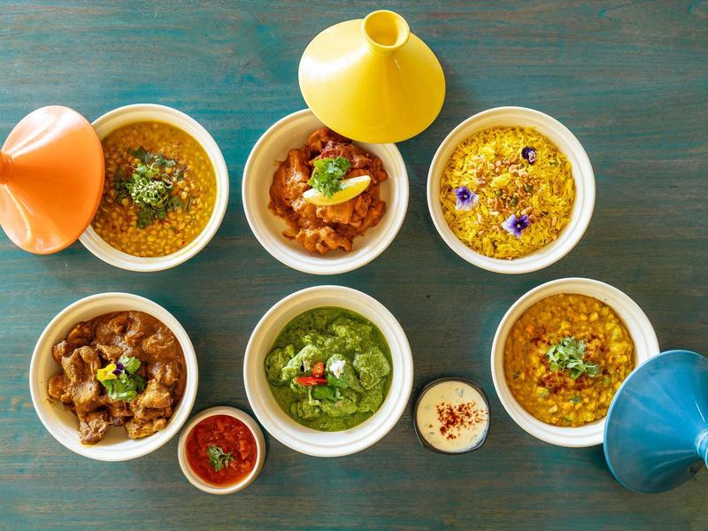 Kolorowe dania tajine w tradycyjnych glinianych garnkach ułożone na stole.