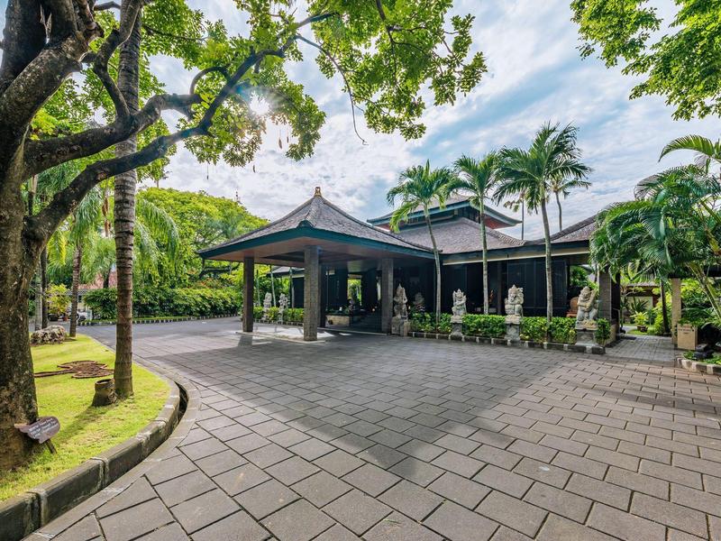 Recepcja hotelowa z zadaszonym wejściem otoczona bujną tropikalną roślinnością.