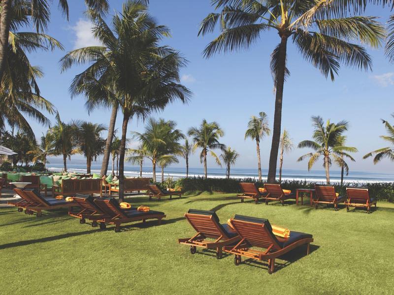 Zielony ogród z leżakami i palmami nad morzem pod błękitnym niebem.