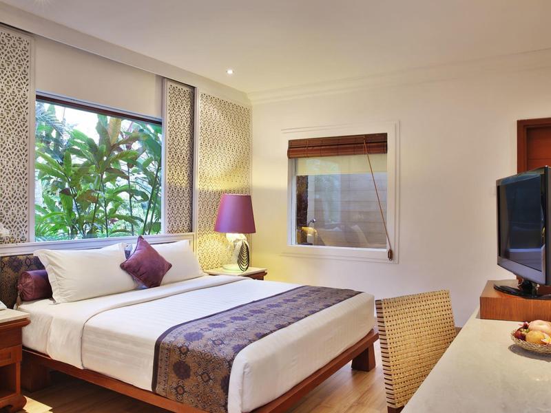 Nowoczesny pokój hotelowy z dużym łóżkiem, telewizorem i oknem z widokiem na zielone rośliny.