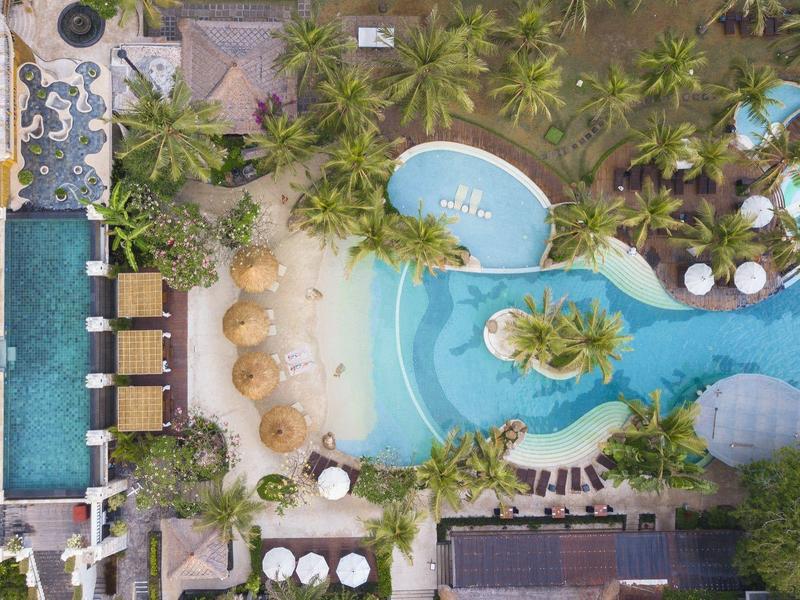 Widok z lotu ptaka tropikalnego basenu hotelowego z leżakami, palmami i lagunowym wzorem.