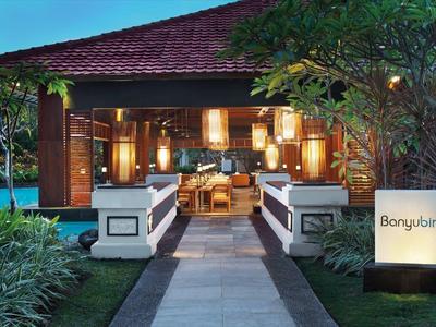 Osvětlená cesta vede k otevřenému pavilonu s posezením, obklopenému bujnou zelení.