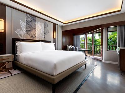 Moderní hotelový pokoj s manželskou postelí, uměleckou výzdobou stěn a balkonem s výhledem na zeleň.